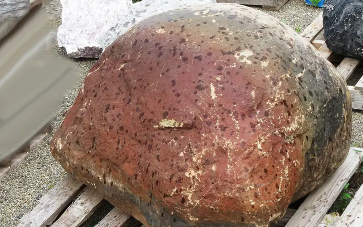 A rounded red boulder with dark speckles