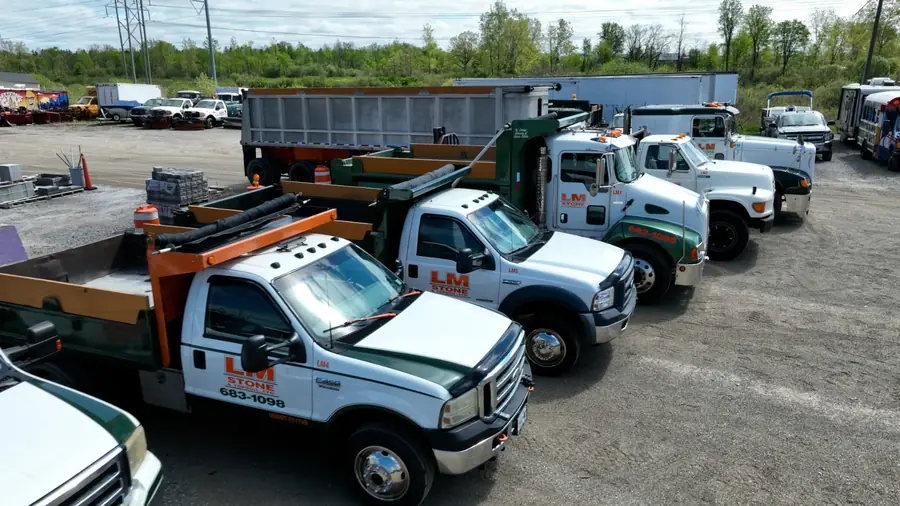 A line of LM Stone dump trucks parked in the yard, green and white with orange LM lettering