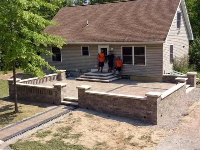 A paver patio with a sitting wall behind a house